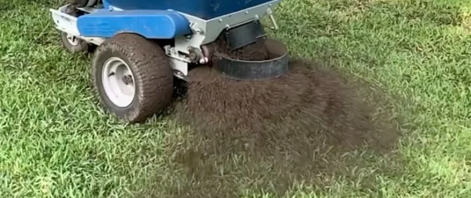 Machine spreading top dressing sand on a lawn in Austin, TX.